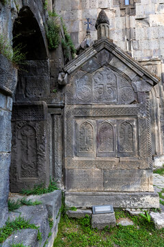 An ornately carved medieval stone tomb decorated with intricate khachkar cross patterns and topped with a gabled roof at the historic Saint Pogos and Petros church, Tatev, Armenia