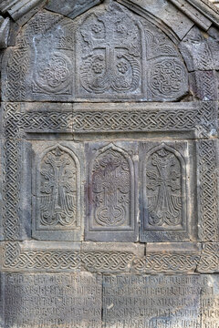 A macro detail of three intricately carved khachkar crosses framed by delicate knotwork and interlace patterns on an ancient medieval stone tomb, Tatev, Armenia