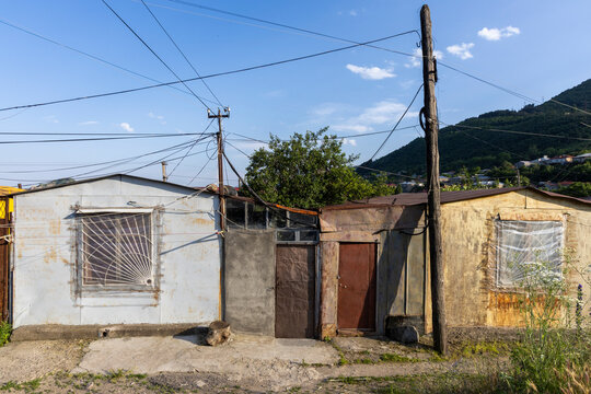 A row of old rustic corrugated metal shacks with rusted doors barred windows and tangled power lines standing weathered and abandoned beneath a blue sky, Goris, Armenia