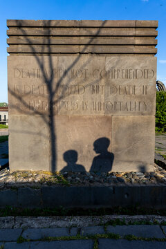 A granite memorial stone engraved with a poetic quote about death and immortality while the silhouetted shadows of two children fall across its surface, Goris, Armenia