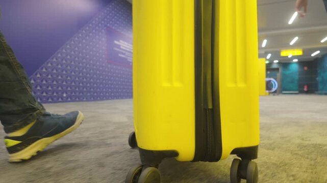 Yellow suitcase on wheels rolling through a modern airport terminal as a person pulls their luggage to the departure gate for their vacation trip or business journey
