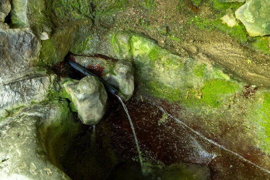 Natural spring water flowing steadily from a simple pipe among moss covered rocks in a quiet forested canyon near the ancient troglodyte village, Khndzoresk, Armenia
