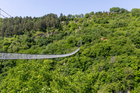 Suspension footbridge made of cable and wood crossing high above a forested gorge and valley under a wide blue summer sky near remote wilderness, Khndzoresk, Armenia