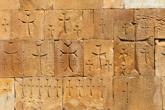 A weathered sandstone wall at the thirteenth century Astvatsatsin church is densely covered with small hand carved khachkar crosses and Armenian inscriptions, Noravank, Armenia