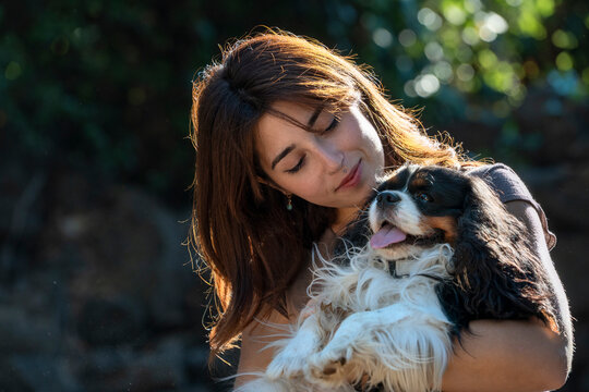 Young woman cuddling her beloved dog outdoors in warm sunlight