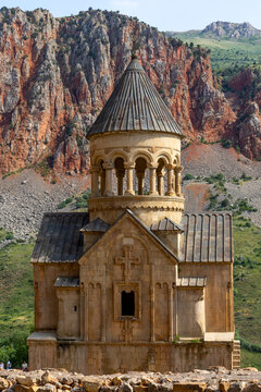 The bell tower of Surb Astvatsatsin church with its rotunda columns and conical roof rises above red rock cliffs at the Noravank monastery under a cloudy sky, Noravank, Armenia