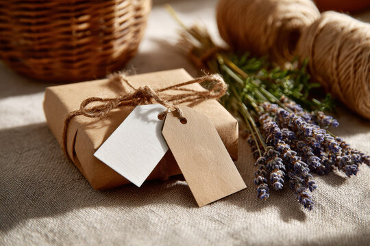 Small kraft paper wrapped gift with paper tags and fresh lavender beside a twine spool and basket
