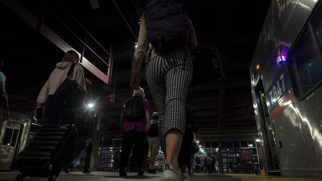 Commuters and travelers walking with luggage on a train station platform at night, preparing for departure or arriving at their destination in an urban city