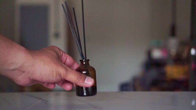 Hand placing scented reed diffuser on a marble countertop indoors. Footage highlighting essential oils, wellness, and calming interior styling.