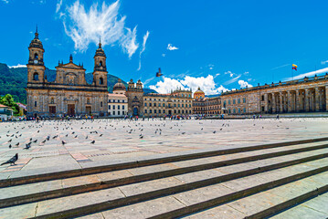 Sunny day at Plaza de Bolivar in Bogota, Colombia, featuring the Primary Cathedral, National Capitol, mountains, and tourists surrounded by pigeons on the historic stone square. © lcrribeiro33@gmail