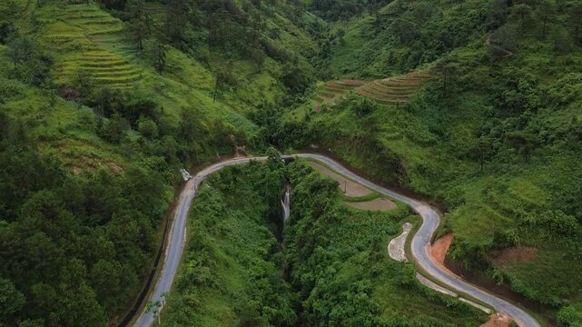 Aerial View of the Crooked Road in The Village, People Riding a Motorcycle, Around Green Forests and Jungles with Palm Trees in Asia, Trees and Rice Fields Among the Mountains