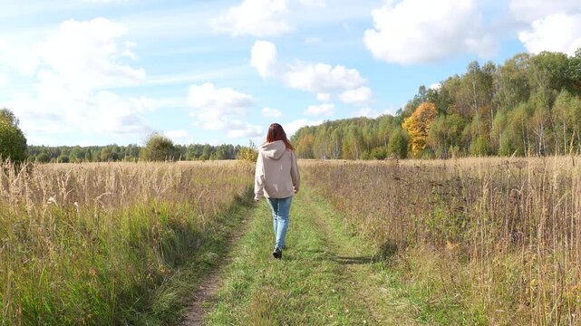 Red-Haired Woman Walking Away on Autumn Village Path Near Tula Russia
A red-haired woman walks away along a quiet village path near Tula, Russia, on an autumn day. Dry grass lines the path, with an au