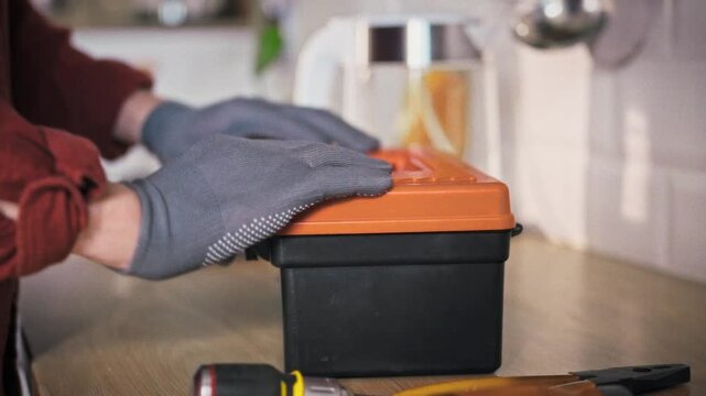 A specialist in uniform sets a toolbox down on a kitchen table in a home environment during the day. Concept of a home repair call and professional technical assistance for household needs