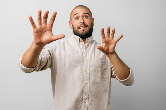 Man caucasian beard young in casual clothes, afraid and terrified, with hand and hands raised in a stop gesture; fear expression, shock and panic, shouting &mdash; studio portrait concept