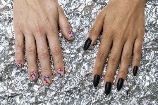 Hands with red and blue nail designs beside matte black nails on crumpled foil