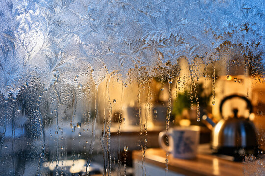 Frost and condensation on glass with a kettle and warm kitchen lights blurred behind