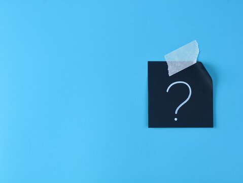Single black adhesive note with a white handwritten question mark taped to blue background with copy space. Concept of FAQ, problem solving, confusion, and business strategy