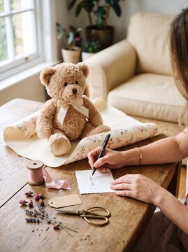 くまのぬいぐるみのプレゼントのそばでメッセージカードを書く人物