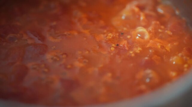 Close-up top view of tomato sauce actively simmering in a metal pot on the stove. Tomato pulp pieces and bubbles visible. Theme of organic homemade sauce and natural food preparation