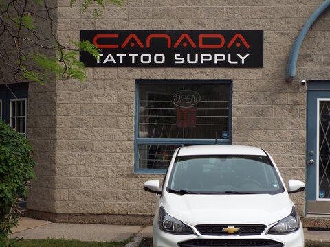 Gloucester, Ontario, Canada &ndash; July 31, 2026: The "Canada Tattoo Supply" storefront sign is mounted above a window on a light-colored masonry commercial building with a parked car at 1010 Polytek St Un