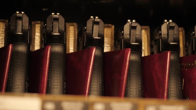Close-up row of handgun grips with burgundy leather cases on dim shelf, warm amber lighting and subtle sliding movement for security display scene