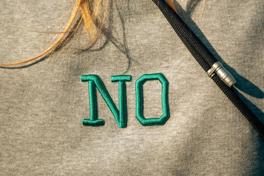 Green embroidered letters spelling the word NO feature prominently on the front chest of a casual grey cotton sweatshirt worn outdoors with blonde hair strand and black drawstring cord detail.