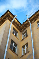 Two metal rain downspout gutters attached to a yellow stucco wall of a classic vintage residential apartment building architecture structure. Old municipal drainage utility system engineering, house.  © Dmitry Presnyakov