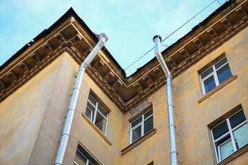 Two metal rain downspout gutters attached to a yellow stucco wall of a classic vintage residential apartment building architecture structure. Old municipal drainage utility system engineering, house.  © Dmitry Presnyakov