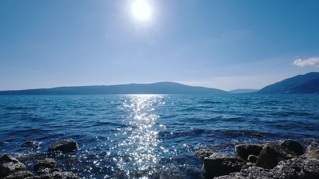 Pan of sunny blue sea coast with mountain landscape and sunlight glare