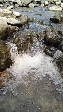 Vertical slow motion clear mountain stream water cascades over rocks into a foamy pool. Freshwater flow concept for ecology, environmental, and splash liquid design background