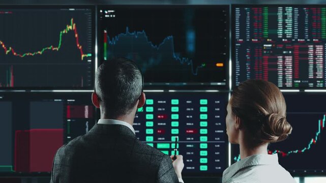 Two traders analysing charts on a wall of monitors. Stock exchange office, teamwork and market research