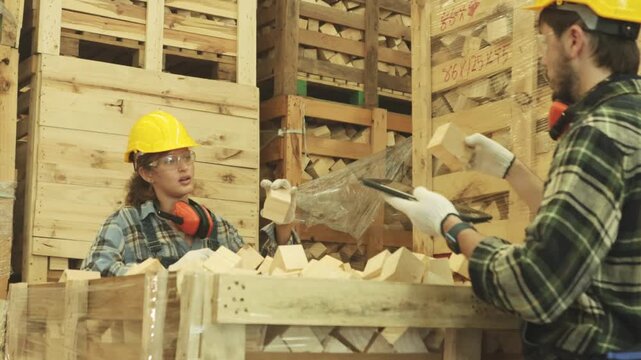 Male and female carpenters inspect hardwood blocks cut into rectangular shapes and stored in wooden crates production pallets must support heavy loads such construction or machinery industries.