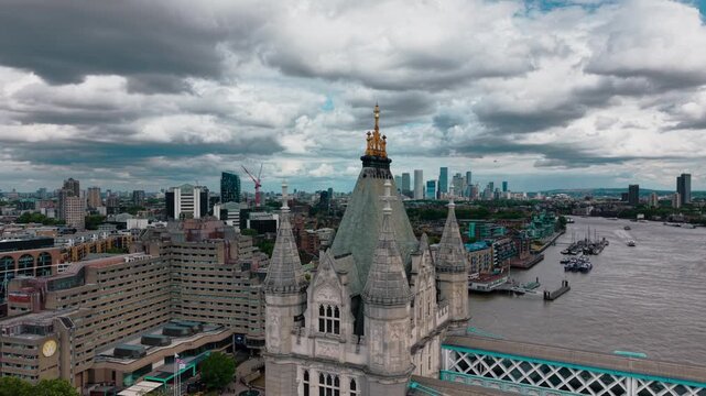 Cinematic aerial view passing close to a historic Tower Bridge tower in London, England, with the River Thames and expansive modern city skyline beneath dramatic clouds