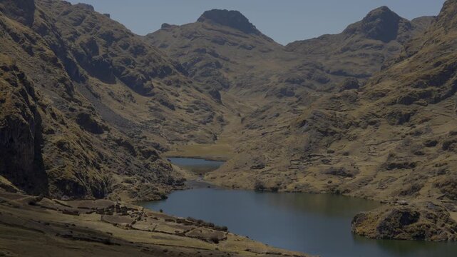 Stunning high-angle panoramic view of a calm blue mountain lake nestled in a rugged Andean canyon in Peru. Dramatic dry peaks, rocky valleys, and remote highlands on a sunny day. Cinematic b-roll.