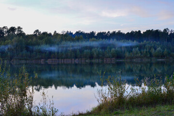 Fototapeta premium Misty Forest Lake at Twilight with fog over lake, front view