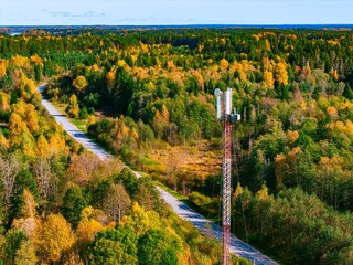 Fototapeta premium Aerial view of a 5G 6G telecommunications antenna tower near a winding rural road in autumn forest