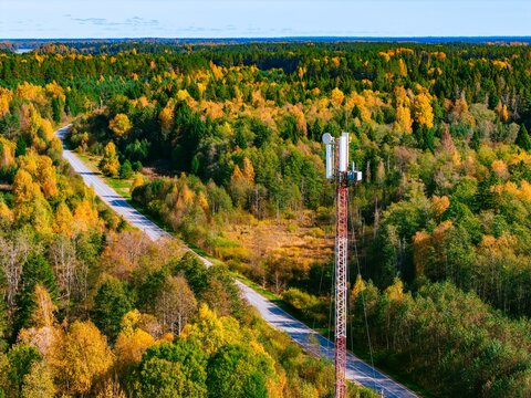Aerial view of a 5G 6G telecommunications antenna tower near a winding rural road in autumn forest