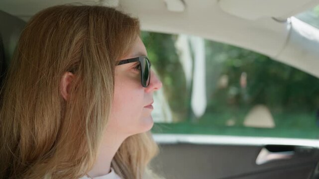 A woman wearing sunglasses is driving a car close up profile sunny day 35 years old