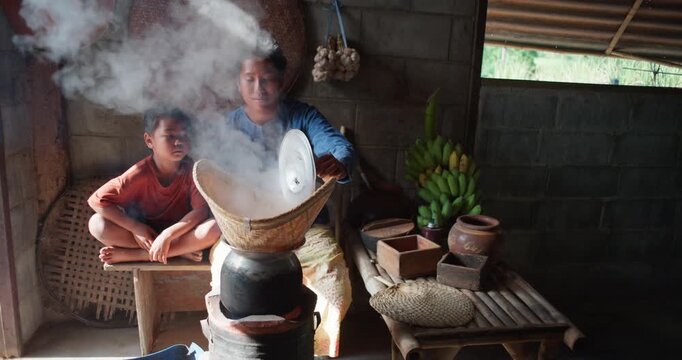 Steam rises from a woven bamboo basket as sticky rice steams over a clay pot, with a daughter sitting nearby in a rural Thai kitchen.