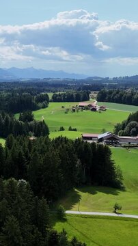 Top view of traditional country houses surrounded by green fields, forests and hills in the foothills of the Alps. Concept of country vacation, farming, sustainable development and European nature