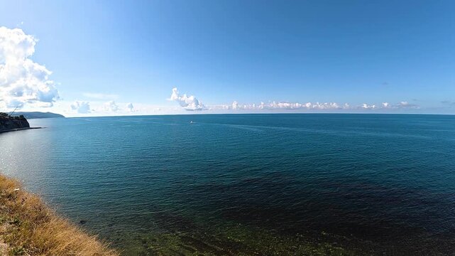 Scenic coastal view featuring a small boat navigating the calm blue waters under a clear sky with scattered clouds and a grassy shoreline in the foreground