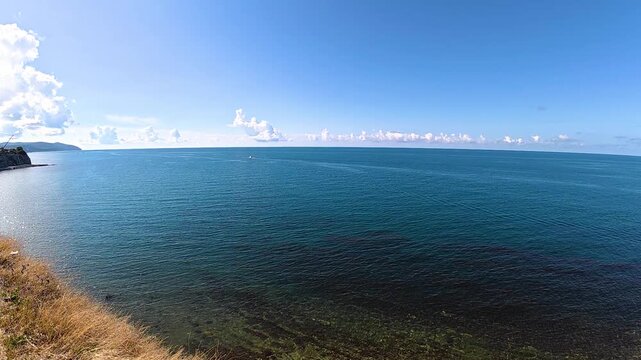 Scenic coastal view featuring a small boat navigating the calm blue waters under a clear sky with scattered clouds and a grassy shoreline in the foreground