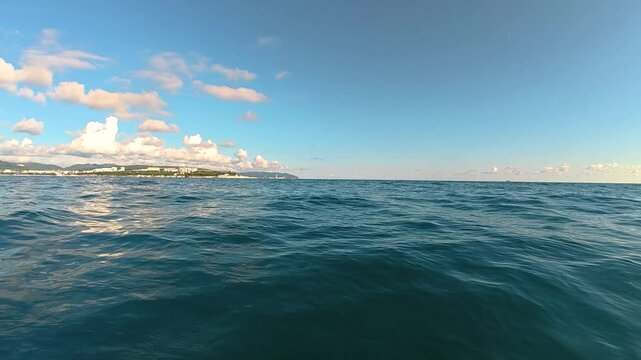 Expansive view of tranquil ocean waters under a clear blue sky with scattered clouds and distant coastal landscape visible along the horizon