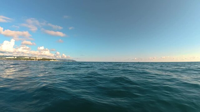 Expansive view of tranquil ocean waters under a clear blue sky with scattered clouds and distant coastal landscape visible along the horizon