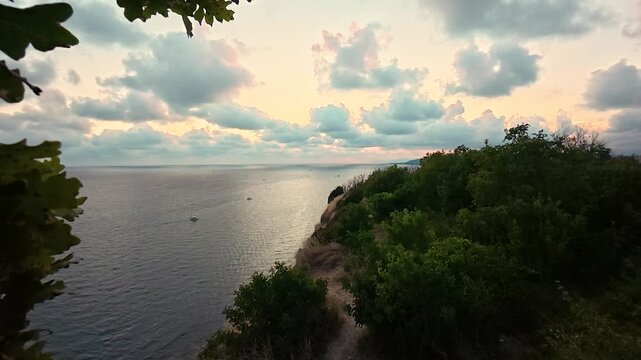 Coastal cliffside path overlooking calm sea beneath glowing sunset clouds and golden dry grass, tranquil natural landscape video