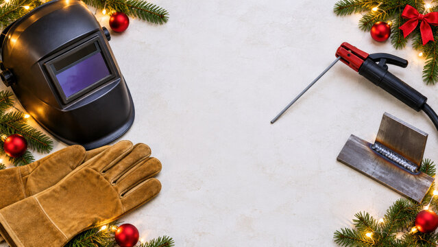 Welding helmet gloves electrode holder and welded steel joint with fir branches - Christmas welder welding background