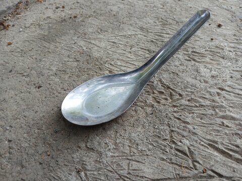 Single metal soup spoon placed on rough gray cement background