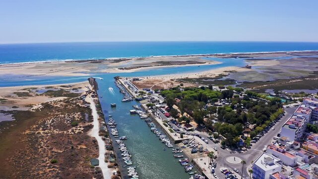 Drone flying backwards revealing the coastal town of fuseta in the algarve region, showing the harbor, the ria formosa lagoon, and the connection to the atlantic ocean on a sunny day