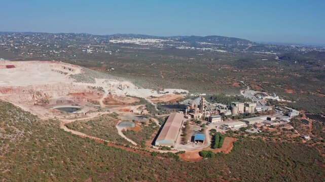 Wide aerial shot revealing a large open pit quarry and an adjacent industrial cement plant, showcasing the scale of the mining and material processing operations in a rural landscape