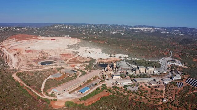 Aerial footage showing a large open pit quarry next to an industrial cement plant with solar panels, highlighting the extraction of raw materials and the production process in a rural landscape